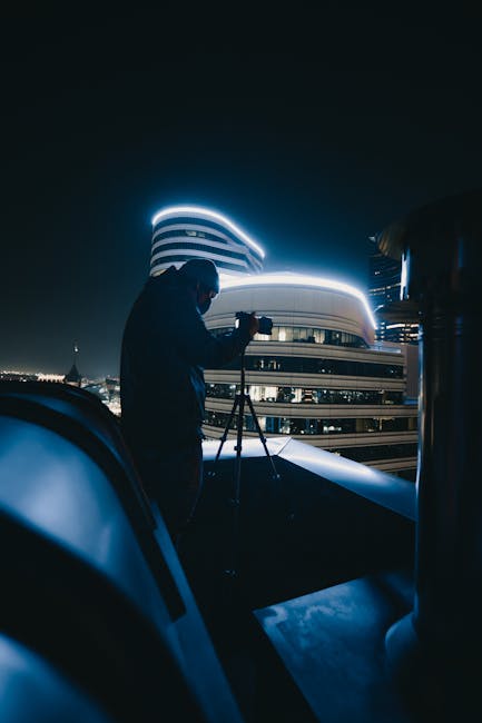 Photographer using a tripod at night with long exposure lighting near buildings and streetlights